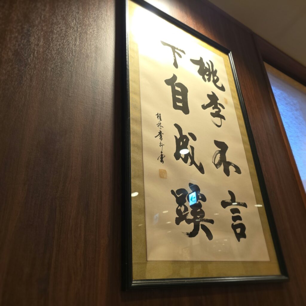 Framed Chinese calligraphy reading 桃李不言 下自成蹊 inside a Bamiyan restaurant