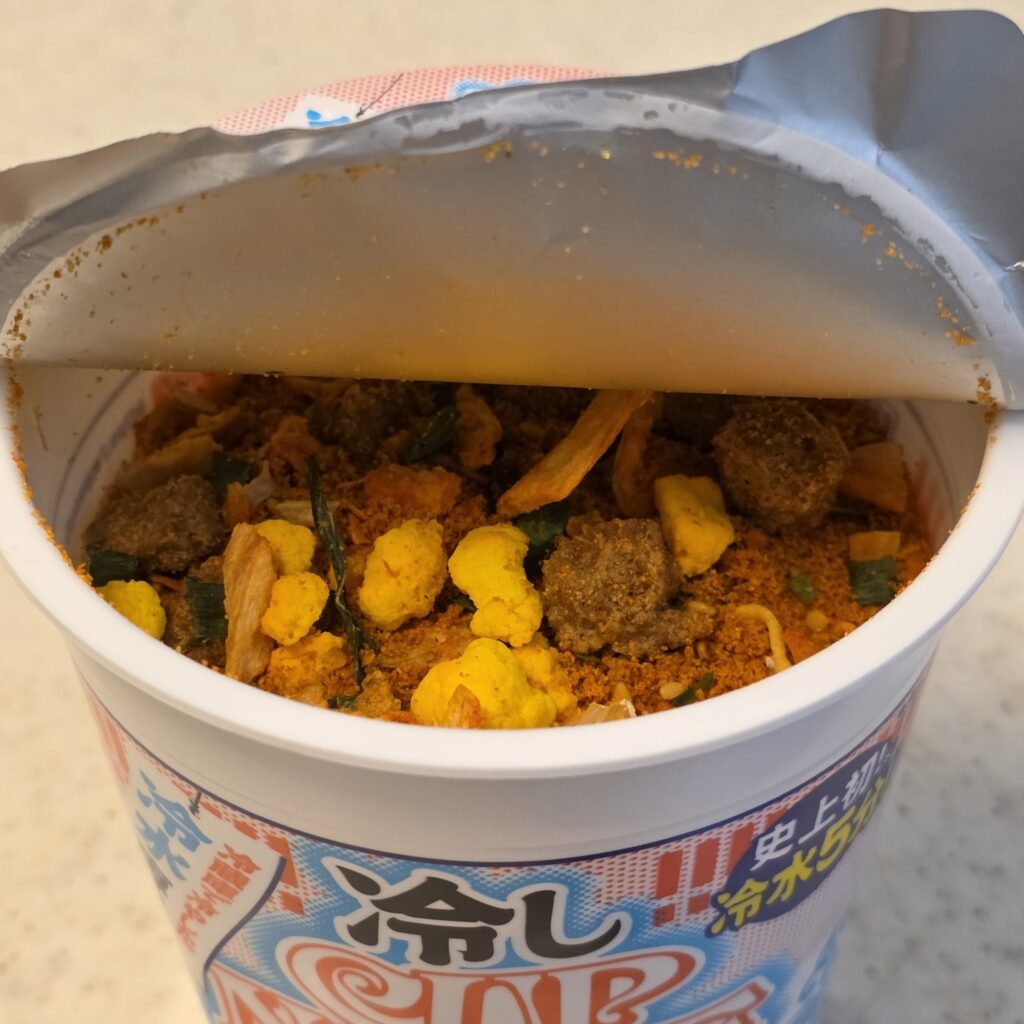 Opened Hiyashi Cup Noodle before adding water, showing dry noodles, seasoning and toppings.