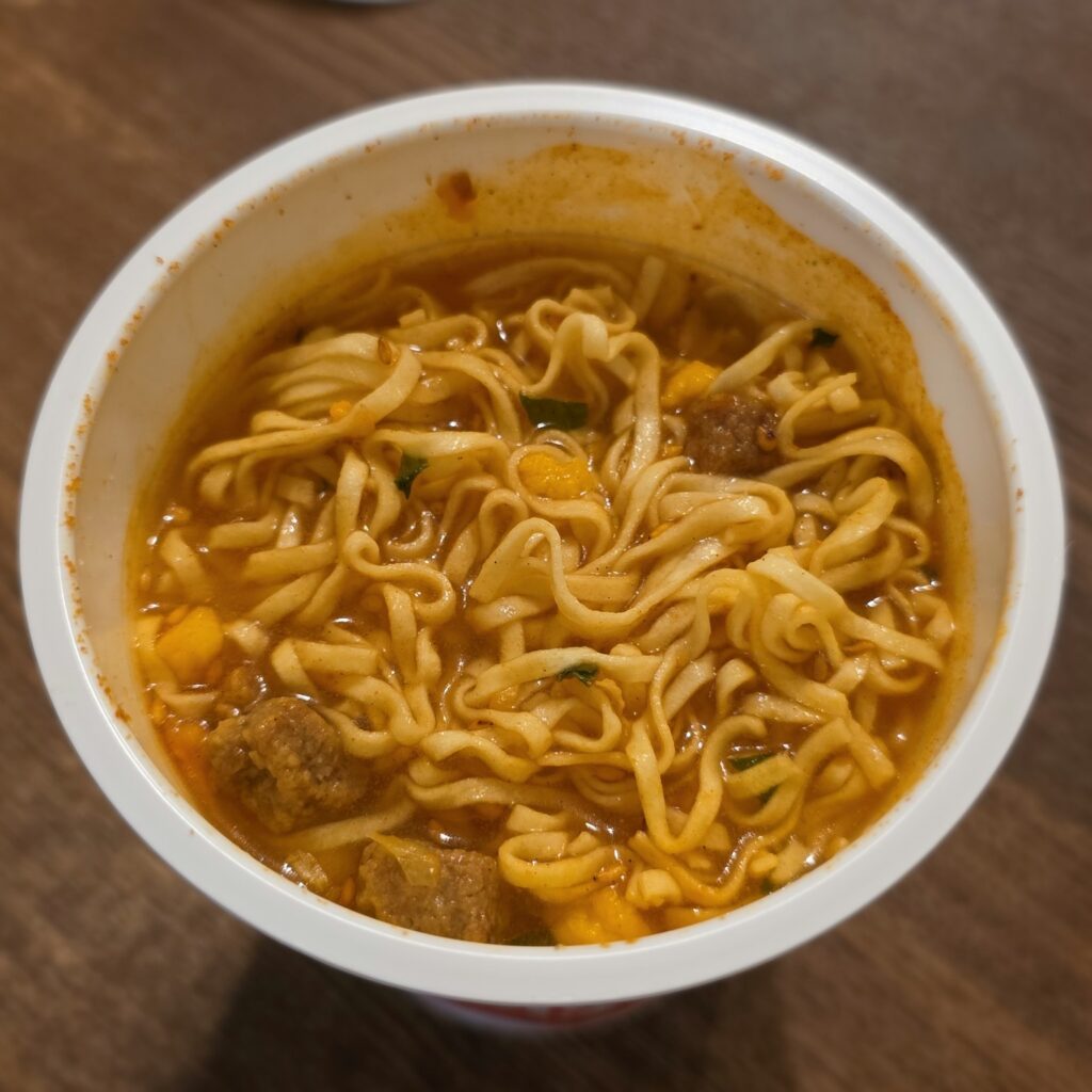 Finished Hiyashi Cup Noodle spicy kimchi flavor after cold-water preparation, viewed from above.