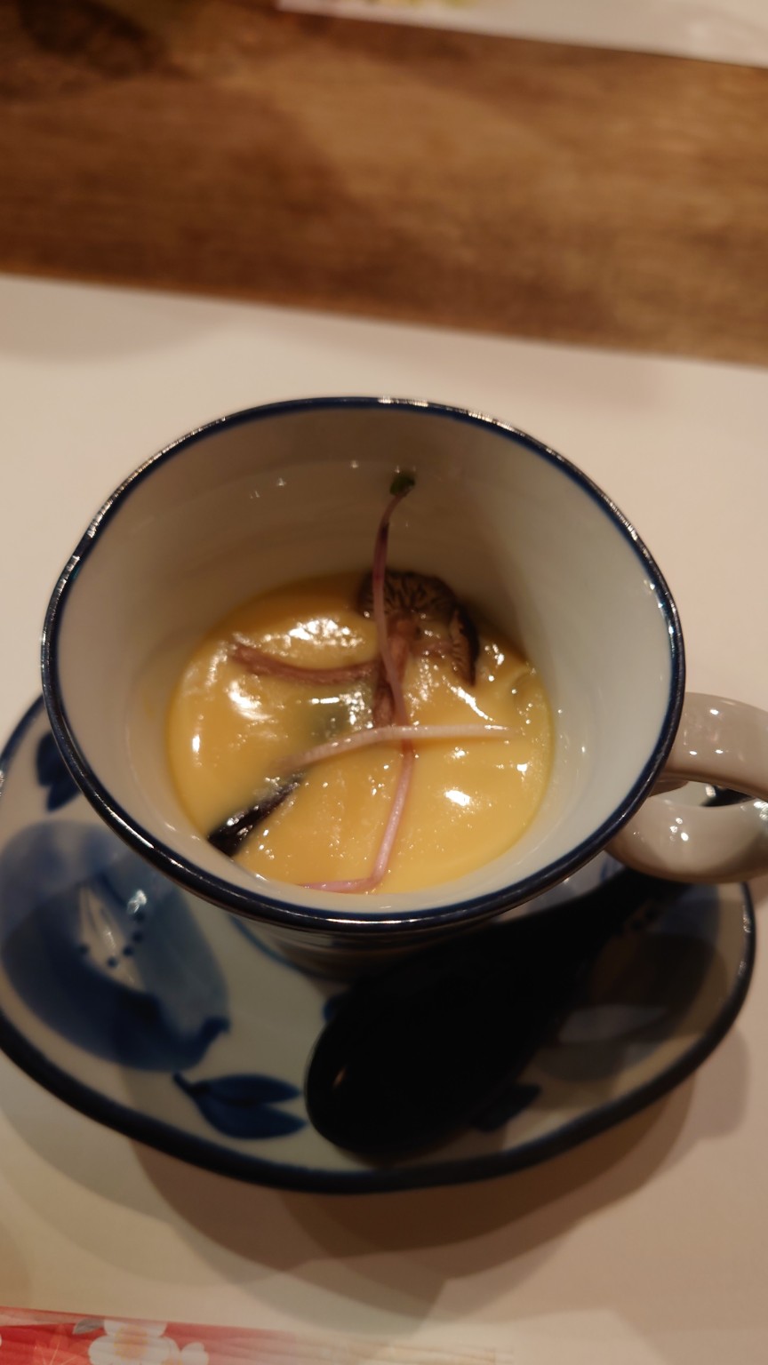 A cup of Japanese chawanmushi, a smooth savory steamed egg custard, served with mushrooms and garnish.