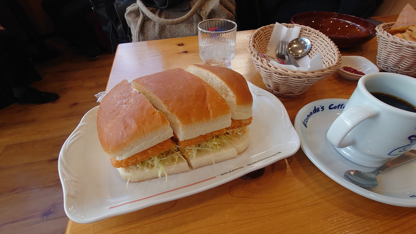 A very large Komeda sandwich served beside a cup of Komeda coffee.