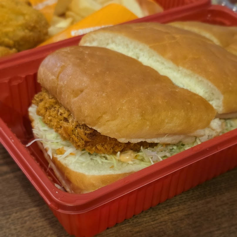 Close-up of a large Komeda Ebi Katsu Pan shrimp-cutlet sandwich in a red takeaway tray.