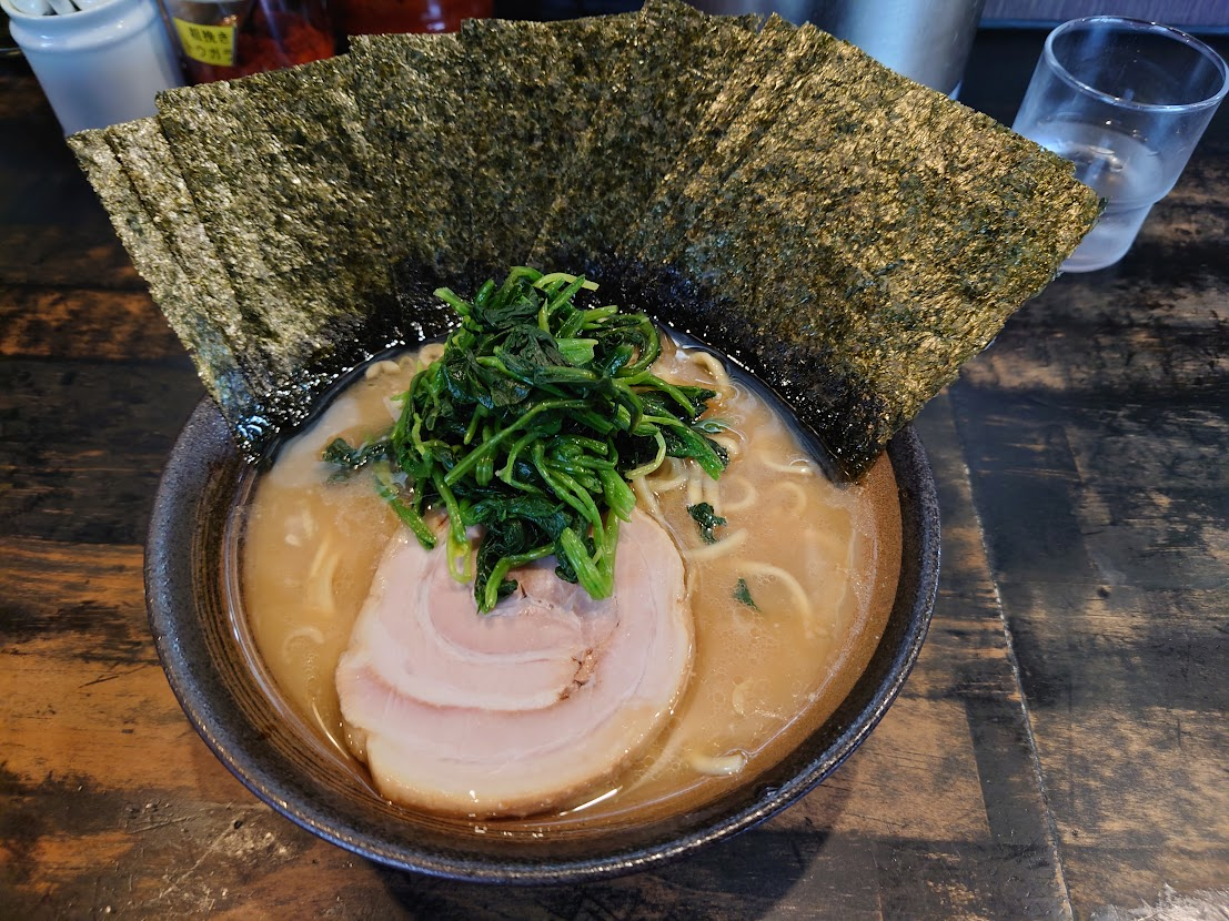 A bowl of Japanese ramen with chashu pork, spinach, and sheets of nori.